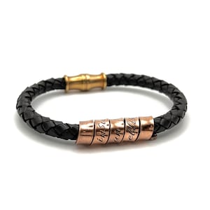May include: A black leather bracelet with a gold clasp and a rose gold bead charm with engraved words.