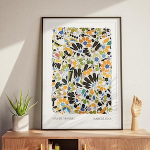 Puede incluir: Impresión artística enmarcada con un diseño de mosaico colorido inspirado en la obra de Gaudí en Barcelona. La obra de arte presenta una vibrante mezcla de formas y colores, incluyendo negro, naranja, azul y verde. La impresión se exhibe en un mueble de madera.