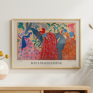 Peut inclure: Une affiche encadrée présentant une illustration colorée avec des personnages vêtus de motifs. L'œuvre, de Baya Mahieddine, comprend du texte en bas. L'affiche est exposée au-dessus d'un meuble en bois avec un vase de fleurs jaunes et une horloge décorative.