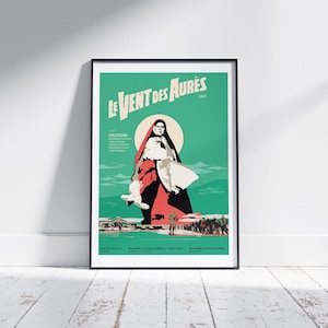 May include: A vintage movie poster for the film "Le Vent des Aurès" (1967) featuring a woman in a red and white dress standing in a desert landscape. The poster is in a black frame.