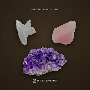 May include: A raw crystal set trio featuring a clear quartz cluster, a pale pink rose quartz stone, and a deep purple amethyst geode cluster. The text RAW CRYSTAL SET · TRIO and BEYOND BOHEMIAN with a logo are printed on the dark brown background.