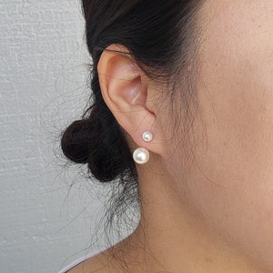 May include: A woman wearing a pair of pearl earrings. The earrings are a classic design with a single pearl on each earring.