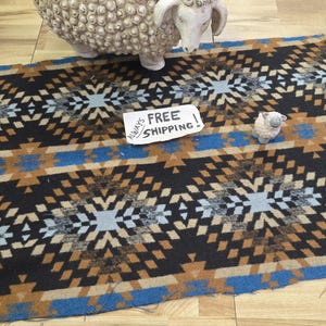 May include: A patterned textile in black, brown, and blue with a geometric design. A small sheep figurine and a larger sheep sculpture are on the textile. A sign that says "FREE SHIPPING" is also on the textile.