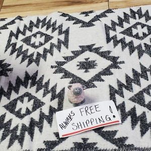 May include: A white and black geometric patterned rug with a fringed edge. A ceramic sheep figurine and a small sheep figurine are on the rug. The rug has a tribal design. The sign says "ALWAYS FREE SHIPPING".