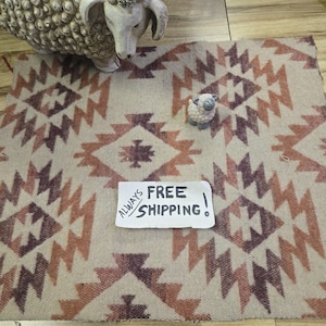 May include: A beige and brown patterned rug with geometric designs. A small sheep figurine and a larger sheep statue are on the rug. The rug has a Southwestern style. The text on the paper says "FREE SHIPPING!"