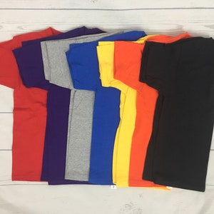 May include: A stack of eight plain t-shirts in various colours, including red, purple, grey, blue, yellow, orange, and black.