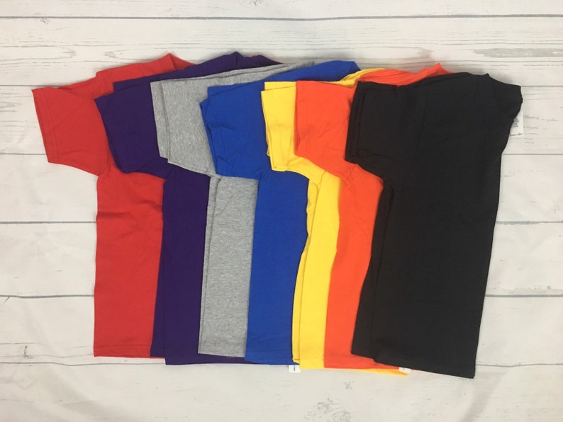 May include: A stack of eight plain t-shirts in various colours, including red, purple, grey, blue, yellow, orange, and black.