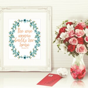 May include: A white framed print with a blue floral wreath and the text "The wise woman builds her house" with the scripture reference "Proverbs 14:1".