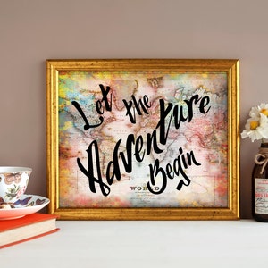 May include: A gold framed print with a vintage world map background and the text "Let the Adventure Begin" in black script. A white teacup with a butterfly pattern sits on a red book next to a vase with white flowers.