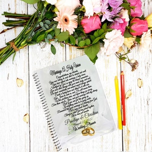 May include: A white spiral bound wedding planner with a floral design and the text "Marriage A Holy Union" and "Penelope & Christian August 22, 2022 Wedding Planner".