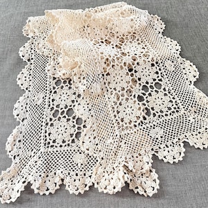 以下が含まれることがあります： クリーム色の手作りのレースのドイリー、スカラップエッジ付き。複雑な透かし彫りのデザインは、花柄と幾何学模様が特徴です。繊細なテキスタイルは、ヴィンテージの装飾に最適な綿またはリネンである可能性があります。