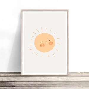 以下が含まれることがあります： 笑顔の太陽のイラストが描かれた、額入りのアートプリント。太陽は明るいオレンジ色で、幸せそうな顔と放射線状の線があります。アートワークは明るい灰色の背景に配置され、明るい木製のフレームに額装されています。