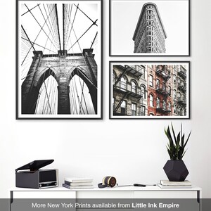 May include: Three black and white framed photographs of New York City. The first photo shows the Brooklyn Bridge from below, the second photo shows the Flatiron Building, and the third photo shows a row of brick buildings with fire escapes.