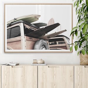 May include: A framed print featuring a vintage wood-paneled station wagon loaded with surfboards. The surfboards are various colors, including light green and natural wood tones. The car has a spare tire mounted on the back. The image is set against a white background.