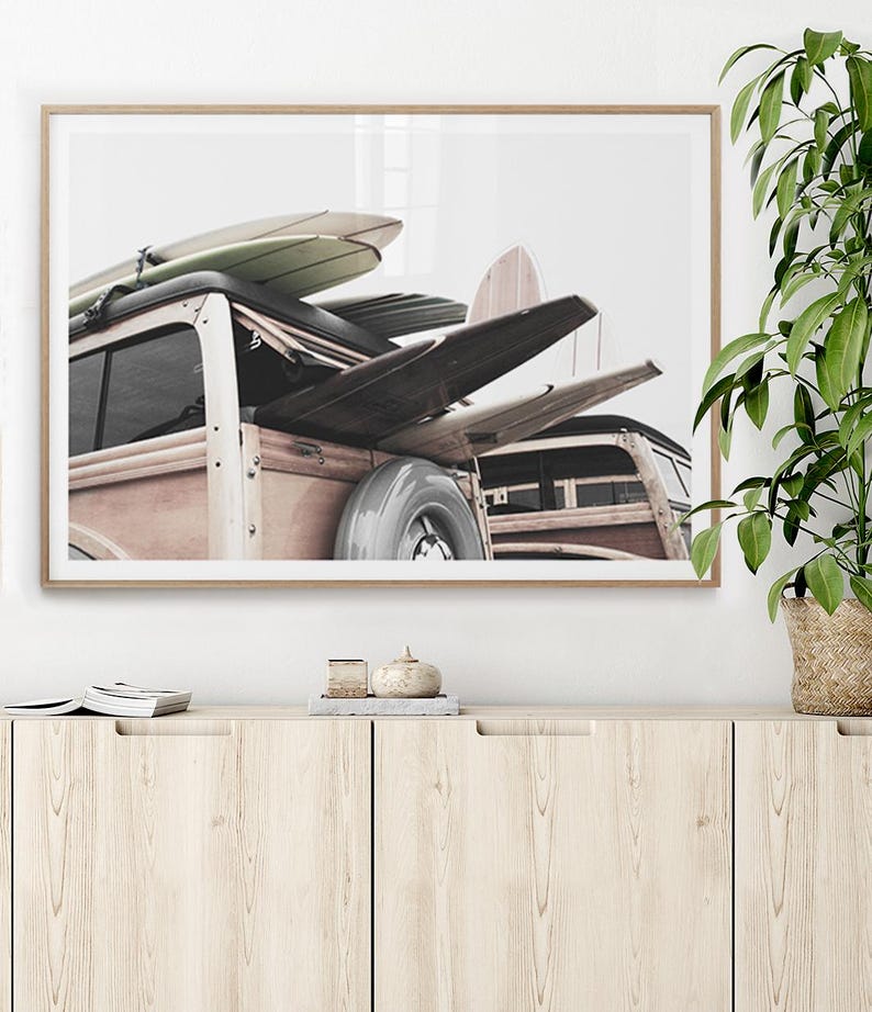 May include: A framed print featuring a vintage wood-paneled station wagon loaded with surfboards. The surfboards are various colors, including light green and natural wood tones. The car has a spare tire mounted on the back. The image is set against a white background.