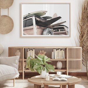 May include: Framed print featuring a vintage wood-paneled station wagon loaded with surfboards. The image has a neutral color palette with a focus on the vehicle and the surfboards. The print is displayed above a wooden cabinet with books and decor.