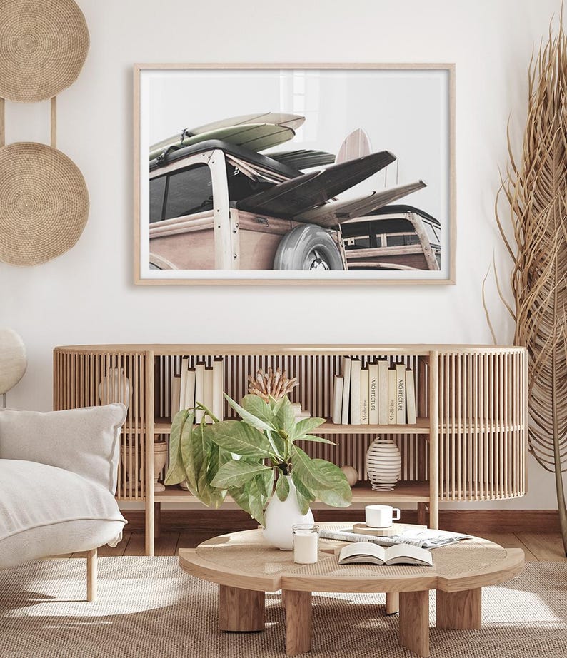 May include: Framed print featuring a vintage wood-paneled station wagon loaded with surfboards. The image has a neutral color palette with a focus on the vehicle and the surfboards. The print is displayed above a wooden cabinet with books and decor.