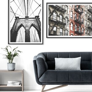 May include: Two black framed prints of New York City. The first print shows a black and white photo of the Brooklyn Bridge. The second print shows a black and white photo of a row of brick buildings with fire escapes.
