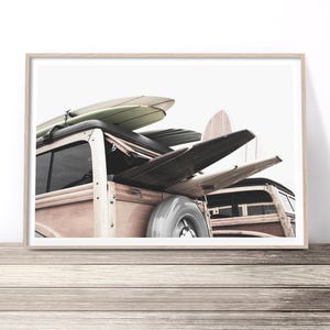 May include: A framed print featuring a vintage wood-paneled station wagon with surfboards strapped to the roof. The surfboards are in various colors and designs. The image is set against a bright white background.