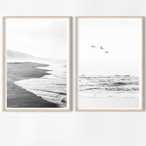 May include: Two black and white framed photographs of a beach scene. The left photo shows a sandy beach with waves crashing on the shore. The right photo shows a view of the ocean with waves and a few birds flying overhead.