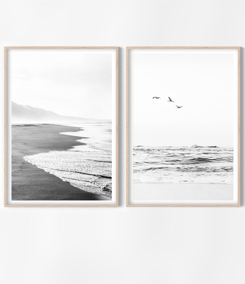 May include: Two black and white framed photographs of a beach scene. The left photo shows a sandy beach with waves crashing on the shore. The right photo shows a view of the ocean with waves and a few birds flying overhead.