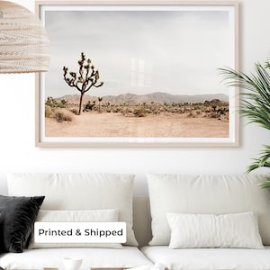 May include: A framed landscape print featuring a Joshua tree in a desert scene. The artwork has a neutral color palette with a light beige frame. The text "Printed & Shipped" is visible on the bottom of the image.