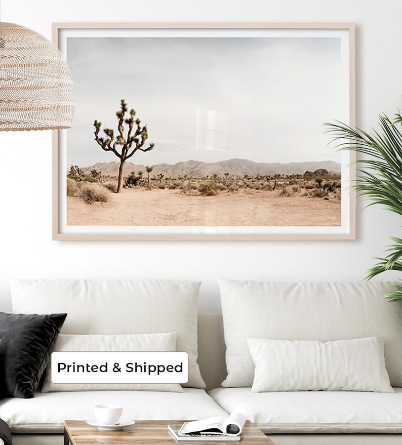 May include: A framed landscape print featuring a Joshua tree in a desert scene. The artwork has a neutral color palette with a light beige frame. The text "Printed & Shipped" is visible on the bottom of the image.