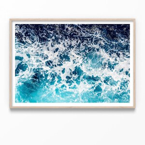 May include: A close-up photograph of a blue ocean with white foam on the surface. The water is a deep blue color, and the foam is white and fluffy. The image is taken from a high angle, looking down at the water.