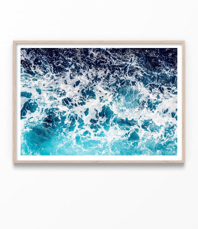 May include: A close-up photograph of a blue ocean with white foam on the surface. The water is a deep blue color, and the foam is white and fluffy. The image is taken from a high angle, looking down at the water.