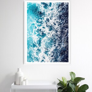 May include: A vertical rectangular wall art print featuring an aerial view of ocean waves crashing against the shore. The image displays a gradient of deep navy blue to bright turquoise water with white sea foam patterns across the surface.