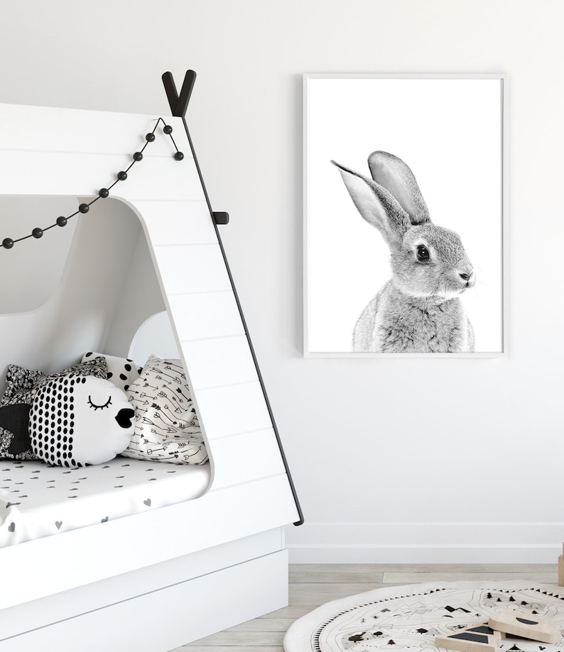 May include: Black and white photograph of a rabbit with its ears perked up, printed on a white frame and hung on a white wall.