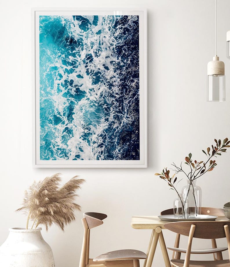 May include: A rectangular wall art print featuring an aerial view of ocean waves crashing against the shore. The image displays a gradient of deep navy blue to bright turquoise water with white sea foam patterns captured in a white frame.