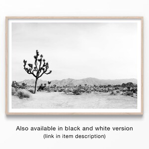 May include: Black and white framed print of a desert landscape featuring a Joshua tree in the foreground. Mountains are visible in the background under a cloudy sky. The print is in a light wood frame. Text at the bottom reads: "Also available in black and white version (link in item description)".