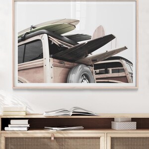 May include: A framed print featuring a vintage wood-paneled station wagon with surfboards strapped to the roof. The surfboards are in various colors and shapes. The print is displayed above a wooden cabinet with books and decorative boxes.