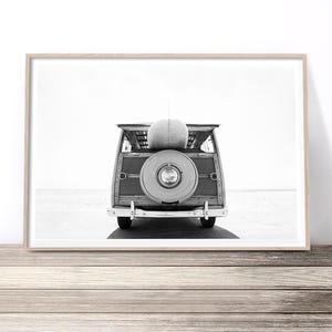 K&ouml;nnte beinhalten: Ein Schwarzwei&szlig;foto eines alten Holz-Kombiwagens mit einem Surfbrett auf dem Dach. Das Auto steht auf einem Strand mit dem Meer im Hintergrund.