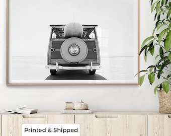 May include: A black and white framed wall art print featuring the rear view of a vintage woody station wagon. The vehicle has a spare tire mounted on the back door and a surfboard resting on the roof rack, set against a bright, minimalist horizon.