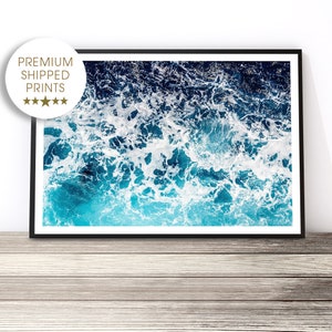 May include: An abstract aerial photograph of ocean waves crashing and creating white foam on the surface of the water. The water is a vibrant blue and turquoise color.