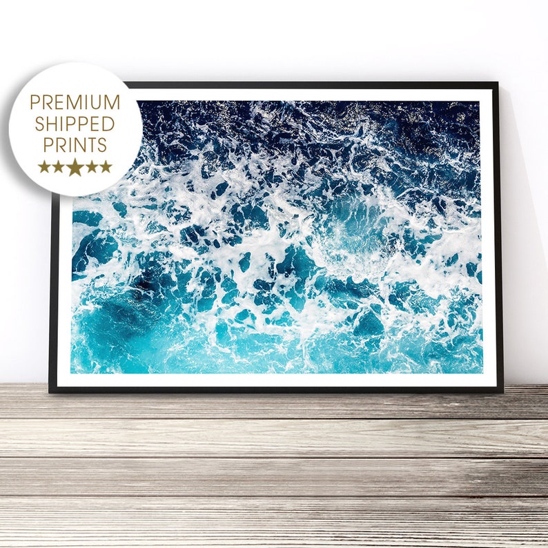 May include: An abstract aerial photograph of ocean waves crashing and creating white foam on the surface of the water. The water is a vibrant blue and turquoise color.