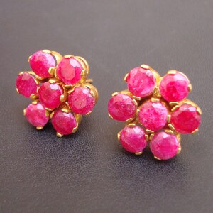 May include: A pair of gold earrings with a flower design. Each earring has seven pink gemstones set in a gold flower shape.