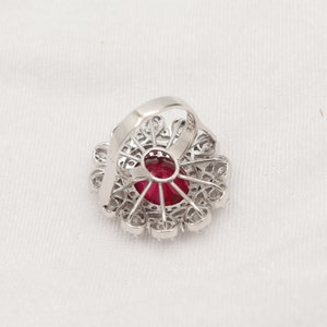 Puede incluir: Un anillo de plata con una gran piedra roja rodeada de piedras peque&ntilde;as transparentes. El anillo tiene un delicado dise&ntilde;o floral.