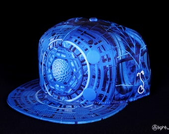 Può includere: Un cappello da baseball blu e bianco con un design geometrico. Il cappello ha una visiera piatta e una corona curva.