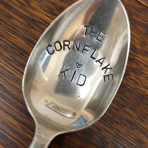 Op de afbeelding: Een zilveren lepel met de woorden "The Cornflake Kid" gegraveerd.