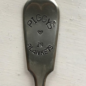 Può includere: Un cucchiaio d'argento con le parole "Piggy's in Blankets" incise sul manico.
