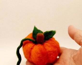 May include: A small, hand-felted orange pumpkin with a green stem and leaves. The pumpkin is about the size of a person's hand.
