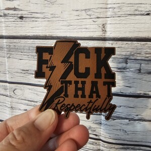 May include: A brown wooden sign with the words "F*CK THAT Respectfully" in black lettering. The word "F*CK" has a lightning bolt design. The sign is held in a person's hand.