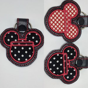 May include: Three black and red fabric keychains with a Mickey Mouse head design. The keychains have white polka dots and red stitching.