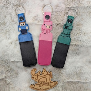 May include: Three keychains with different characters from the video game Minecraft. The keychains are made of fabric and have a black backing. The characters are Steve, a pig, and Creeper.