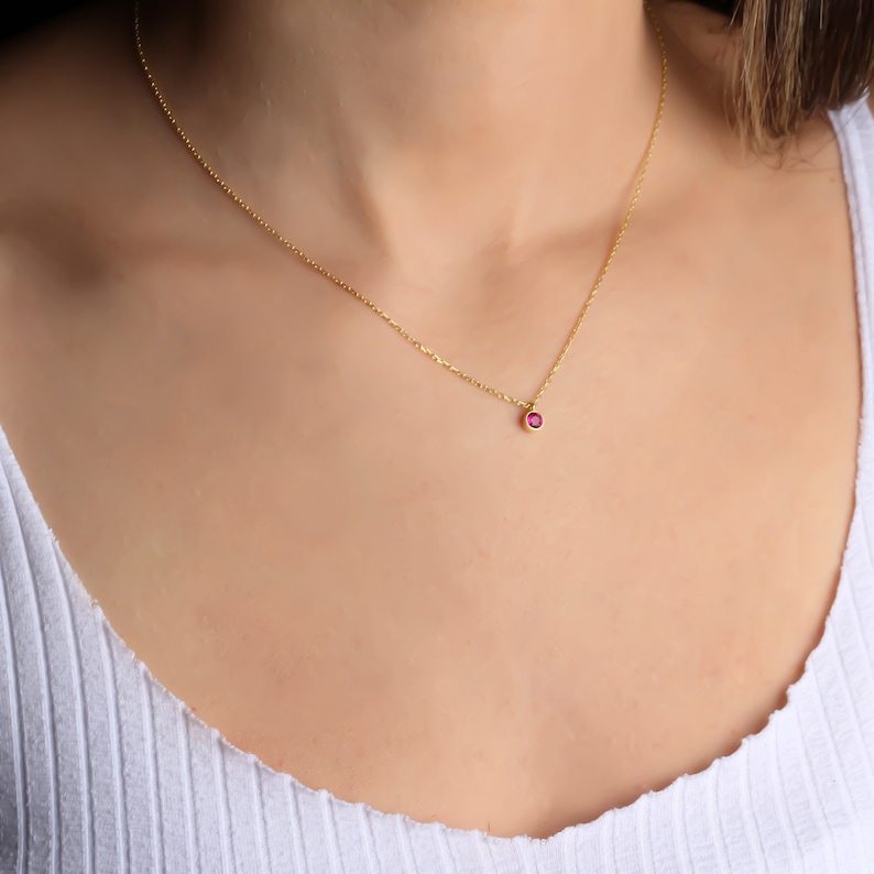 May include: A delicate gold chain necklace with a small, round, red gemstone pendant.