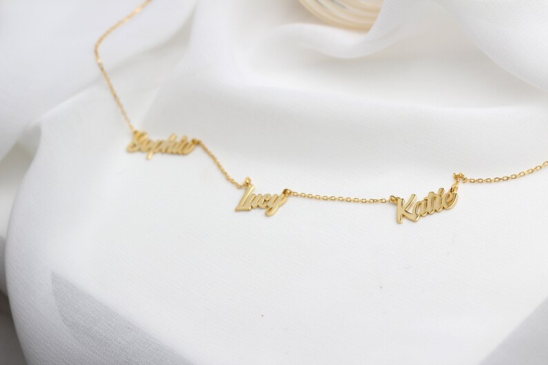 May include: A gold necklace with three names, "Sophie", "Lucy", and "Katie", spelled out in cursive.