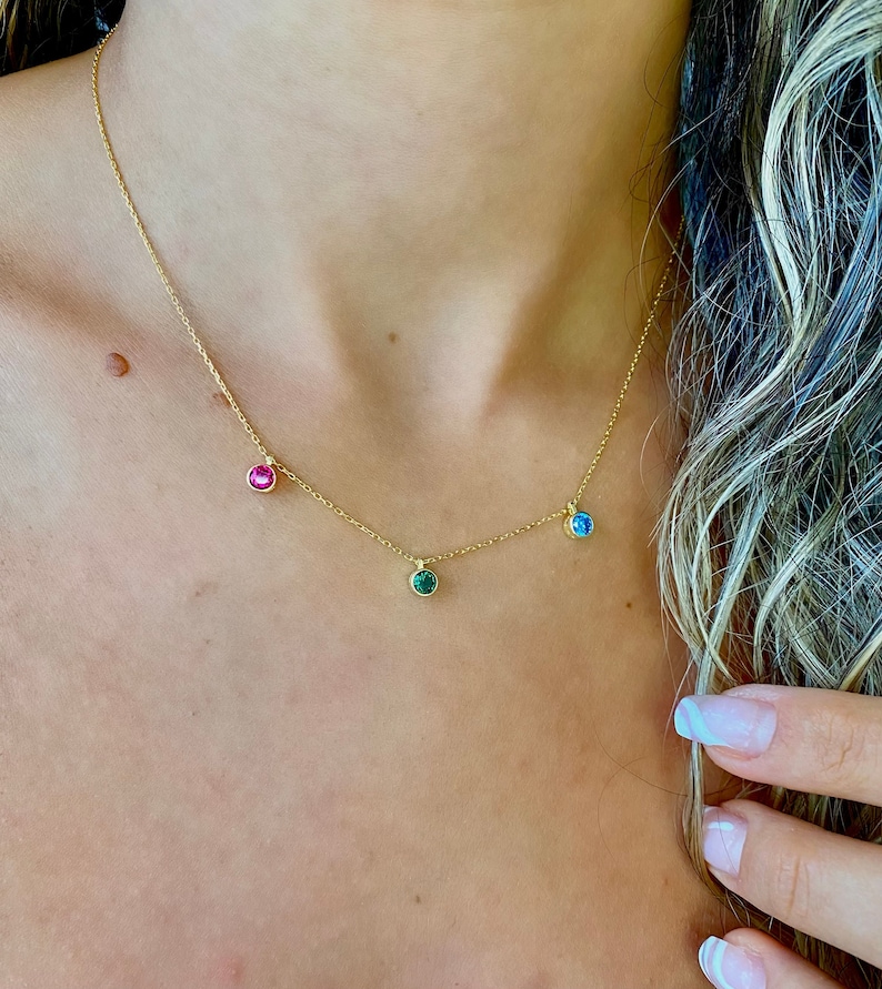 May include: A gold chain necklace with three small round gemstones. The gemstones are pink, green, and blue.